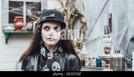 Belle petite fille effrayante célébrant halloween. Terrifiant noir, blanc demi-visage maquillage et costume de sorcière, image élégante. Horreur, plaisir chez les enfants Banque D'Images