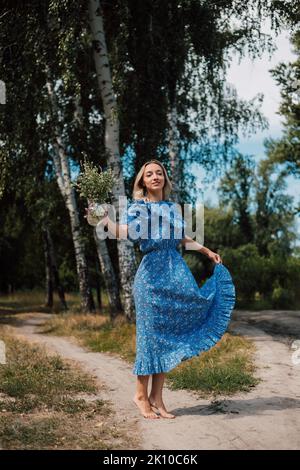 Une jeune femme attrayante avec des fleurs entre ses mains marche à travers la forêt Banque D'Images