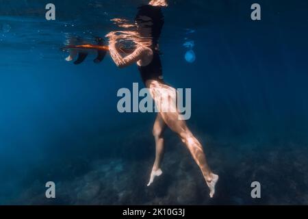 Surfeur nageant à bord en mer bleue. Vue sous-marine avec femme et planche de surf Banque D'Images
