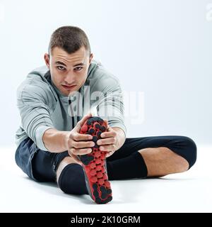 Si cela ne vous défie pas, cela ne vous changera pas. Un jeune homme assis dans un studio tout en faisant des étirements. Banque D'Images