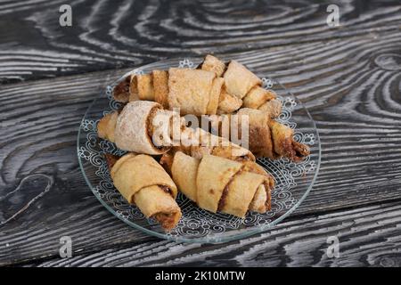 Croissants à la cannelle. Petits pains à la cannelle. Ils se trouvent sur une soucoupe. Arrière-plan de planches de pin noir. Gros plan. Banque D'Images