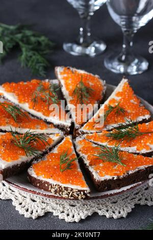 Sandwichs maison avec caviar rouge sur une assiette de pain de seigle sur fond gris, en-cas festif Banque D'Images