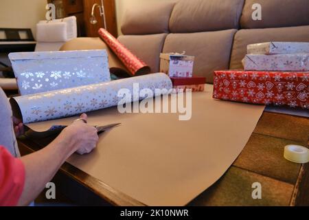 Une femme méconnue qui coupe du papier de Noël pour emballer des cadeaux. Banque D'Images