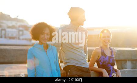 Profitez d'une course matinale revigorante. Portrait de trois amis prenant une pause sur le côté de la route pendant un jogging du matin. Banque D'Images