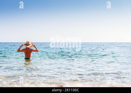 Belle femme blonde dans un chapeau de paille debout dans la mer sur une plage à Corfou Banque D'Images