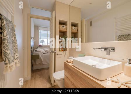 Salle de bains avec meuble-lavabo en bois avec miroir sans cadre, alcôve avec étagères et lavabo en porcelaine blanche Banque D'Images