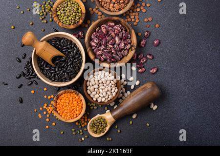 Vue de dessus de différents haricots, lentilles, mung ou maash dans des bols sur fond de béton foncé Banque D'Images