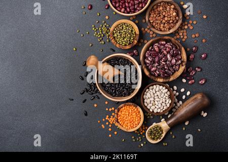 Vue de dessus de différents haricots, lentilles, mung ou maash dans des bols sur fond de béton foncé Banque D'Images