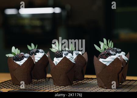Petits gâteaux au chocolat décorés de crème au beurre et de baies sur la table. Le produit fini Banque D'Images