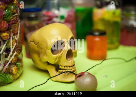 Gros plan du crâne avec des bonbons et autres friandises dans un endroit frais et couvert Halloween Party Spread. Des idées de décoration simples et traditionnelles. Arrière-plan horizontal amusant. Banque D'Images