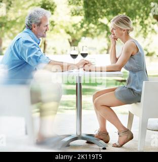 Se détendre dans l'entreprise. Heureux couple mature assis à une table avec deux verres de vin tout en tenant les mains à l'extérieur. Banque D'Images