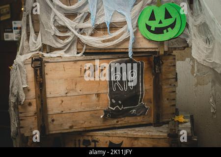 Citrouille d'halloween lumineuse verte avec nez, bouche et yeux peints sur une boîte en bois avec gaze comme toile et pierre tombale avec inscription RIP. Images faites main Banque D'Images