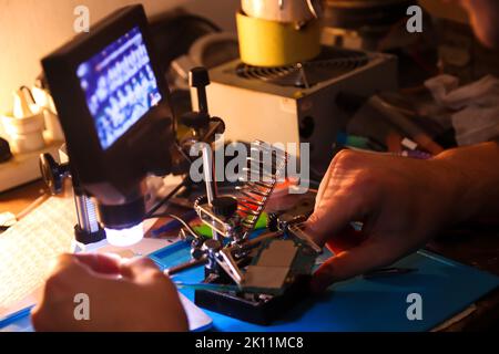 Flou artistique de la main mâle avec un microscope. Travailler avec un fer à souder. Appareil microélectronique. Gros plan des mains d'un technicien de maintenance qui répare un smartphone moderne Banque D'Images