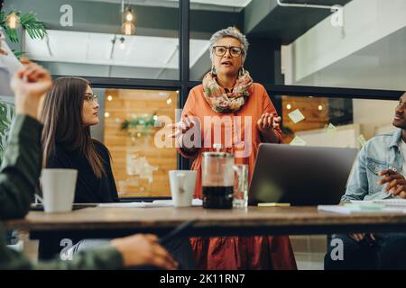 Femme d'affaires mature dirigeant une réunion dans un bureau créatif. Femme d'affaires expérimentée partageant sa stratégie avec ses collègues. Groupe de multicultura Banque D'Images