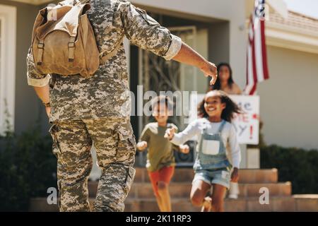 Des enfants enthousiastes qui s'étreilssent pour embrasser leur père. Un père militaire reçoit un accueil chaleureux de sa femme et de ses enfants à la maison. Retour d'un soldat américain Banque D'Images