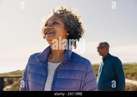 Femme sénior souriant gaiement tout en regardant une vue rafraîchissante sur un pont à pied. Bonne femme âgée qui profite de vacances reposantes au bord de la mer Banque D'Images