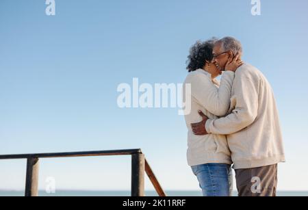 Les oiseaux de rivage mûrs étant romantiques à la plage. Heureux couple senior s'embrassant en se tenant sur un pont de pied en bois. Couple de personnes âgées à la retraite Banque D'Images