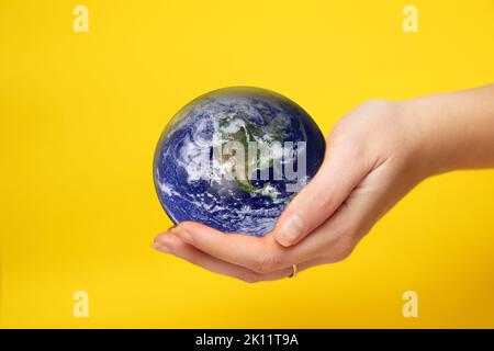 Flou artistique de la main féminine tenant le globe terrestre sur fond jaune. Concept de protection de l'environnement. La terre entre les mains. À l'exception de la Terre. Éléments de cette image Banque D'Images