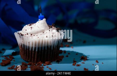 cupcake au chocolat avec crème au beurre blanc et bougie bleue, fond foncé et ruban bleu Banque D'Images