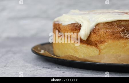 gros plan de la glaçage à la crème au beurre sur le gâteau au rouleau de cannelle, fond blanc, table en marbre gris Banque D'Images