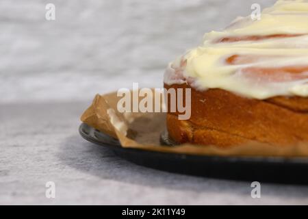 gros plan de la glaçage à la crème au beurre sur le gâteau au rouleau de cannelle, fond blanc, table en marbre gris Banque D'Images