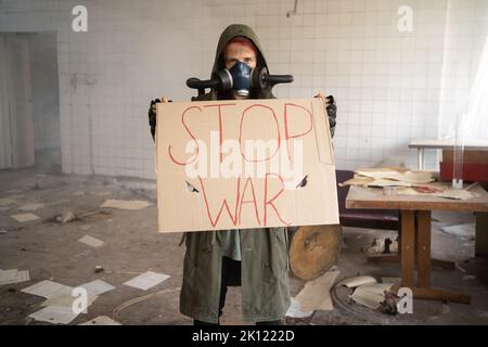 Une femme portant un écriteau No War avec un signe dans une manifestation de protestation contre la guerre. Fille en ruiné portant un masque à gaz, abandonné bâtiment détruit. Post apoca Banque D'Images