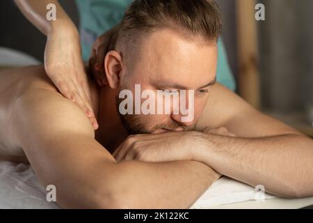 homme charmant et détendu, qui se fait masser au spa. jeune homme barbu, qui se trouve au spa moderne pour hommes, qui s'est posé sur une table de massage et qui se guérit Banque D'Images