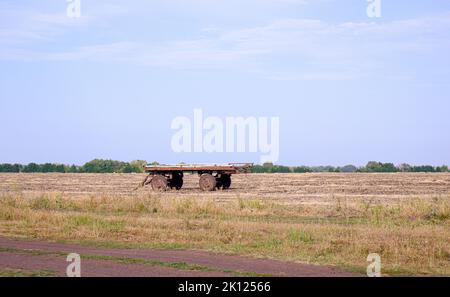 Ancien chariot vide pour recueillir la paille dans le champ. Equipement de récolte dans un champ de blé rustique. Banque D'Images