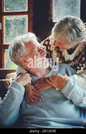 Un couple de personnes âgées heureux s'enharche et profiter de temps ensemble à la maison assis sur une chaise longue et se souriant les uns les autres. Concept des personnes âgées relation mûre. Joie re Banque D'Images