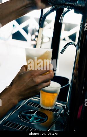 Gros plan de la bière servie à la main dans le verre à l'aide du robinet. Le barman verse de la bière tout en se tenant au comptoir du bar. Main de Barman à la bière pression verser une abeille à la pression Banque D'Images