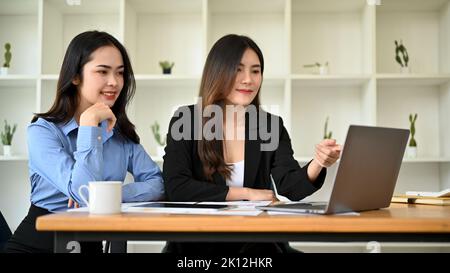 Deux employés de bureau asiatiques talentueux et charmants travaillant ensemble sur leur projet, discutant et partageant leurs idées. Banque D'Images