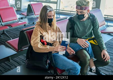 Jeune couple de touristes élégants assis dans un aéroport vide avec des passeports dans leurs mains. L'homme et la femme caucasiens attendent leur vol Banque D'Images