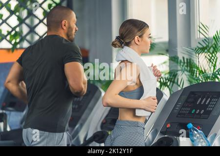 vue d'un jeune homme et d'une femme sur le tapis roulant à la salle de gym, plan moyen. Photo de haute qualité Banque D'Images