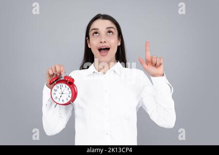 Fille tenant un réveil montre. Portrait d'une jeune femme drôle et belle avec un réveil debout sur fond gris. Banque D'Images