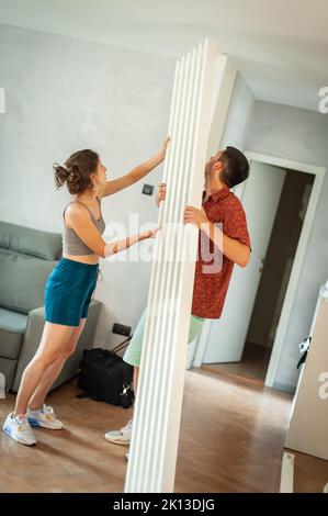 Cohabitation. Un jeune couple marié installe une poutre décorative dans son nouvel appartement Banque D'Images