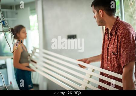 Cohabitation. Un jeune couple marié installe une poutre décorative dans son nouvel appartement Banque D'Images