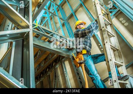 L'entrepreneur caucasien escalade une échelle à l'intérieur de la construction de cadre de maison en acier pendant ses travaux de développement. Nouveau bâtiment de l'unité commerciale. Banque D'Images