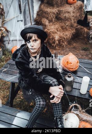 Belle petite fille effrayante célébrant halloween. Terrifiant noir, blanc demi-visage maquillage et costume de sorcière, image élégante. Horreur, plaisir chez les enfants Banque D'Images