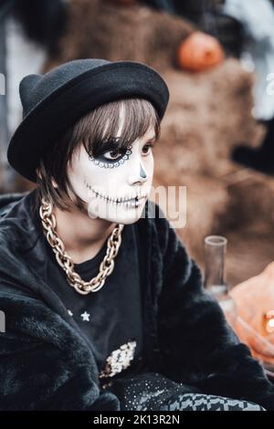 Belle petite fille effrayante célébrant halloween. Terrifiant noir, blanc demi-visage maquillage et costume de sorcière, image élégante. Horreur, plaisir chez les enfants Banque D'Images