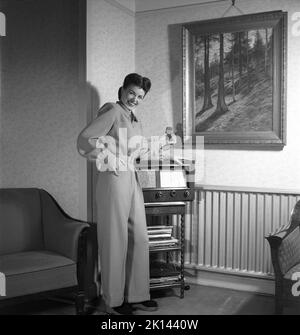 La mode des femmes en 1940s. Une jeune femme photographiée pour un magazine de dames pour montrer la mode féminine de 1945. Le modèle féminin porte une combinaison à pantalon. Elle se penche sur un typique de l'époque, la radio à transistor. Suède 1945. Kristoffersson Réf. R5-1 Banque D'Images