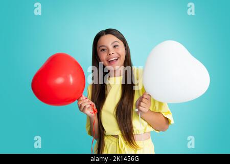 Jolie petite fille de l'adolescence jouant avec le ballon en forme de coeur rouge. Visage de fille heureux, émotions positives et souriantes. Banque D'Images