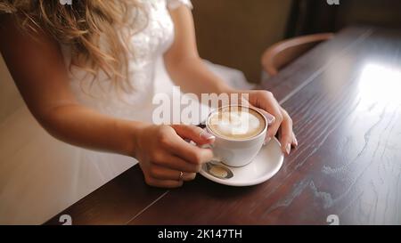 Une jolie femme boit du cappuccino au restaurant. Temps de café pour la mariée au mariage. Banque D'Images