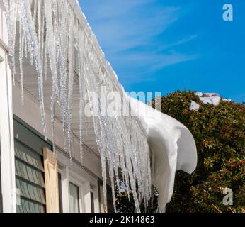 quelques jours après une tempête de neige, des glaces pendent du toit d'une maison tandis que la neige fond avec le ciel bleu au-dessus. Banque D'Images