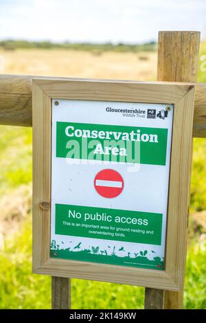 Panneau de conservation sur une clôture en bois britannique devant un champ avec un fond de ciel bleu estival. Banque D'Images