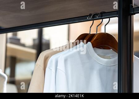 Les chemises sont accrochées dans un placard de marche avec un T-shirt beige et blanc. Banque D'Images