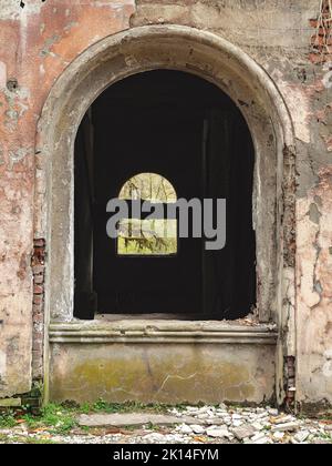 Ouverture de fenêtre voûtée d'un bâtiment abandonné en lambeaux. Banque D'Images