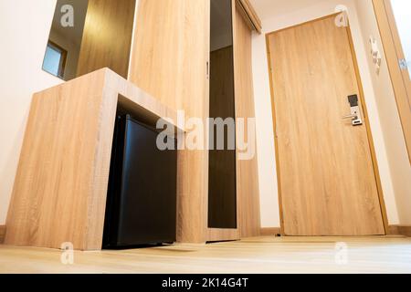 Le petit réfrigérateur situé sous un comptoir en bois dans une chambre d'hôtel est fermé. Ce réfrigérateur minimaliste est de couleur noire. Banque D'Images