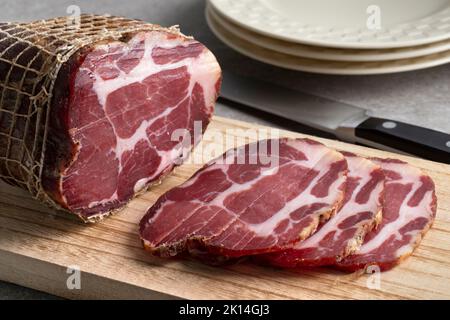 Morceau de porc fumé séché traditionnel croate, bacon de collier de porc, et des tranches de gros plan sur une planche à découper Banque D'Images