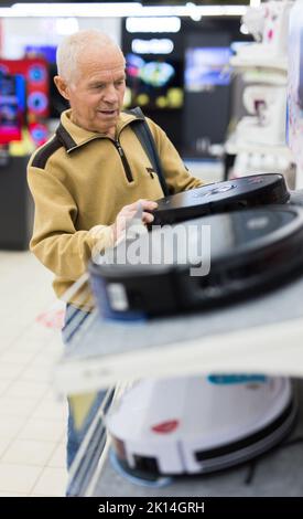 Sénior homme retraité achetant un aspirateur robotique dans la salle d'exposition du magasin d'appareils électriques Banque D'Images