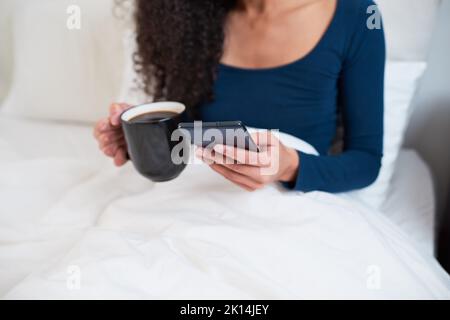 Gros plan d'une femme au téléphone portable au lit tout en buvant du café noir Banque D'Images